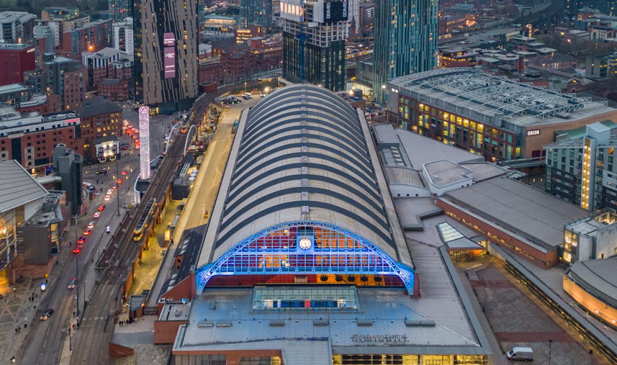 An daytime aerial drone shot showing a birds eye view of Manchester Central and the surrounding skyscrapers and city.